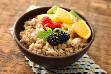 Tasty oatmeal with berries and fruit in bowl on table