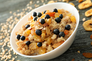 Tasty oatmeal with berries and dried fruits in bowl on table, closeup