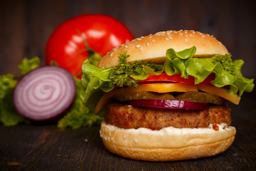 big fresh tasty burger with vegetables on a dark wooden table, cheeseburger, fast food