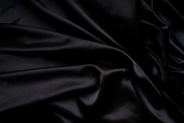 Dark black silky, satin  fabric, wave, draperies. Beautiful textile backdrop. Close-up. Top view 