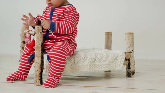 child sits on a small wooden bed in red striped pajamas