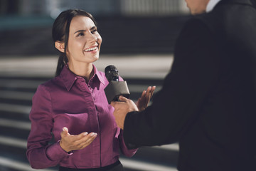 A woman with a smile on her face answers the question. A man holds a microphone listening to an...