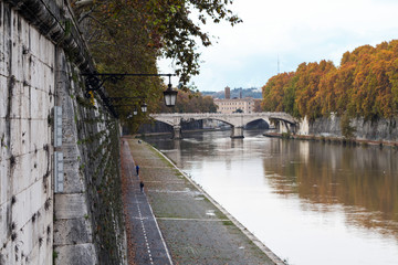 Fototapeta na wymiar Rome, Italy - river Tiber - embankment, autumn day. Few people walking and running along quay