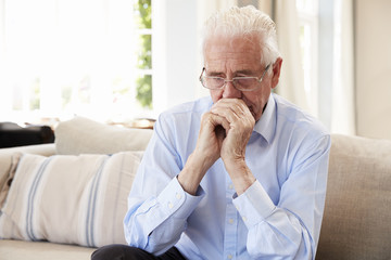 Senior Man Sitting On Sofa At Home Suffering From Depression