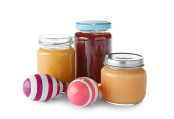 Jars of yummy baby food and rattles on white background