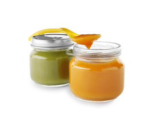 Jars with yummy baby food and spoon on white background
