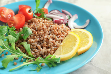 Plate with tasty buckwheat porridge and vegetables on table, closeup