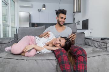 Man Use Cell Smart Phone with Woman Lying On His Knees, Happy Young Couple Together On Couch In Modern Apartment Communicating In Social Media