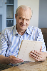 Senior Man Sitting At Home Using Digital Tablet At Table
