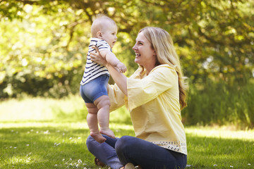 Young Mother Playing With Baby Son Outdoors In Summer Garden