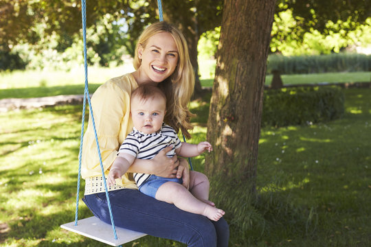 Portrait Of Mother Playing With Baby Son On Garden Swing