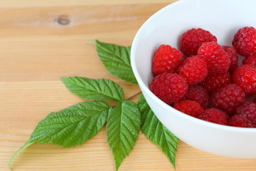 fresh red raspberry fruits in a small white bowl