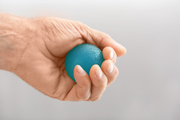 Hand of senior man doing exercise with rubber ball on blurred background