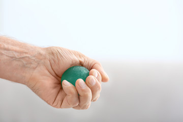 Hand of senior man doing exercise with rubber ball on blurred background