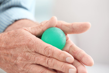 Hands of senior man doing exercise with rubber ball on blurred background, closeup