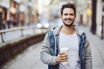 Portrait of smiling man holding coffee with city street in background