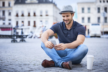 Man sitting on city square using phone