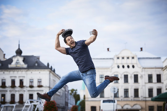 Man jumping and taking selfie holding fedora hat