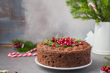 Traditional Christmas English pudding (fruit cake) with rosemary and cranberries on white plate on a concrete light background. Christmas decor of the table.  