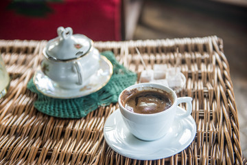 Strong Turkish style coffee in a cup on awooden table with turkish delight and sugar pot in a background