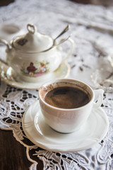Strong Turkish style coffee in a cup on a table with sugar pot in a background
