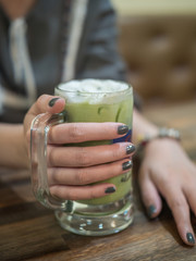 Woman hand holding iced green tea in the coffee shop