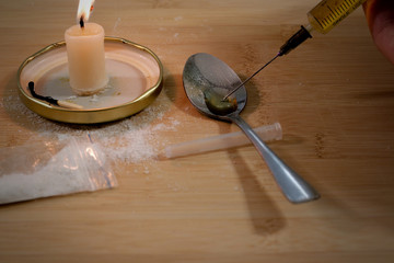 Drug syringe and cooked heroin on spoon. Cocaine in the bag, scattered. Candle burns. Evening.