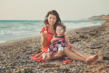 Hokum tender scene of beautiful adorable young mother enjoy life time summer vacation with her little baby girl daughter on sand beach.Family emotions together