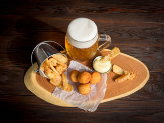 Snacks to beer. Llight beer, fried potatoes, sauce, cheese balls on a dark wooden background. Top view