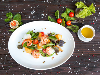 Fresh salad plate with shrimp, tomato and mixed greens on dark wooden  background. Healthy food. Clean eating. Top view.