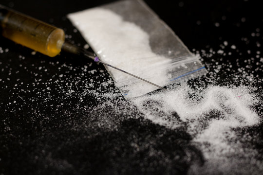 Drug syringe and cooked heroin. Cocaine in the bag, scattered. Isolated on a black background.