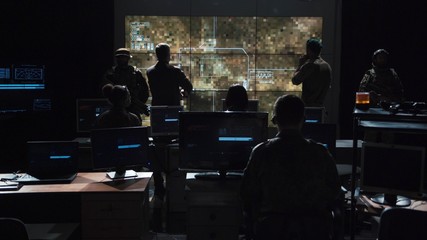 Group of soldiers or spies in dark room with large monitors and advanced satellite communication technology launching a missle. Includes flashing yellow light. - obrazy, fototapety, plakaty