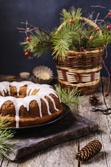 Christmas Bundt Cake with icing, basket with pine branches, pine cones, candles on vintage wooden table. Christmas table decoration. Selective focus 