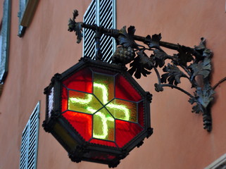 Schmiedeeiserne, rot-gelb verglaste Straßenlaterne an einer Apotheke in der Altstadt von Bologna
