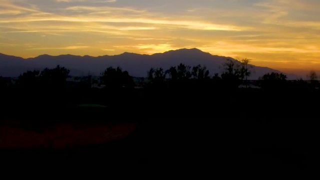 Ascending aerial shot of the sunset behind mountains on the horizon