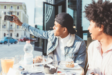Young multiethnic couple sitting bar taking selfie with smart phone  - vanity, social network, technology concept