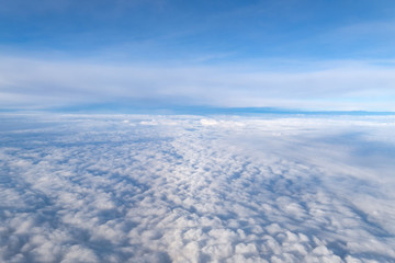 View from airplane window above the clouds with blue sky and cloudscape in sunlight morining. white wispy cirrus and cirrostratus clouds