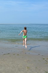 Fototapeta na wymiar Mädchen im Bikini am Sandstrand , rennt ins Meer