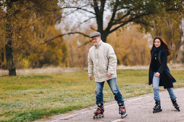 The old man goes on rollers with his daughter in the autumn park. Happy pension. Active old people.The old man goes on rollers with his daughter in the autumn park. Happy pension. Active old people.