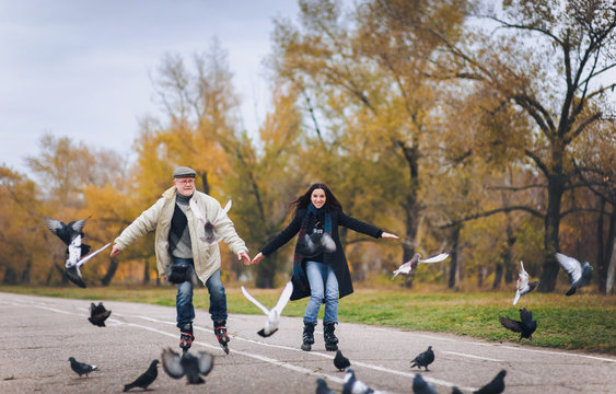 An elderly man and his daughter have fun skating on roller skates. People spreading hands. People and pigeons.