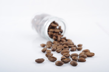 roasted coffee beans poured from clear glass on white background closeup