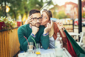 Woman sitting in cafe with handsome man and colorful shopping bags, cup of coffee, holding credit card. On line shopping concept. Beautiful couple smiling.