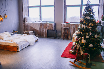 Large beautiful Christmas tree stands before bright windows in the bedroom