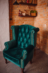 Large soft green armchair stands before a brick wall in cosy room
