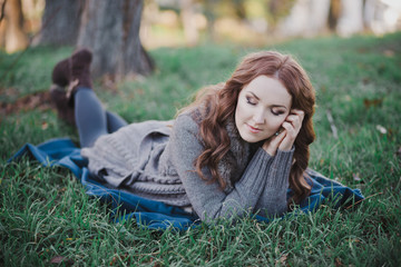 Sensual brunette lady with pout pink lips and white cheeks wearing casual cosy sweater with fur posing sit for on green grass in autumn forest central park