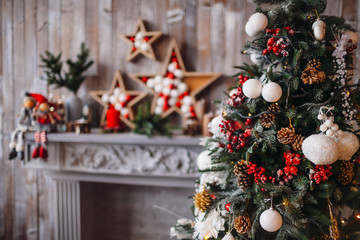 Beuatiful Christmas tree rich decorated with toys stands over presents before a fireplace in cosy bright room