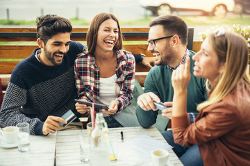 Group of four friends having fun a coffee together. Two women and two men at cafe talking laughing...