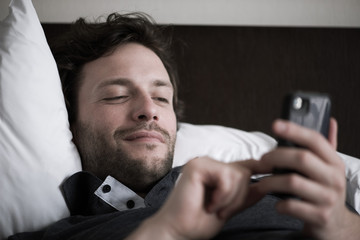 Man reclining in bed using smart phone