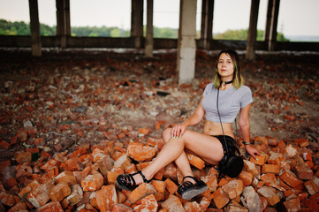 Girl wear on shorts at abadoned factoty sitting on brick.