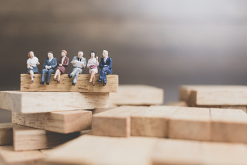 Miniature people : Business People sitting on wood block with wooden background